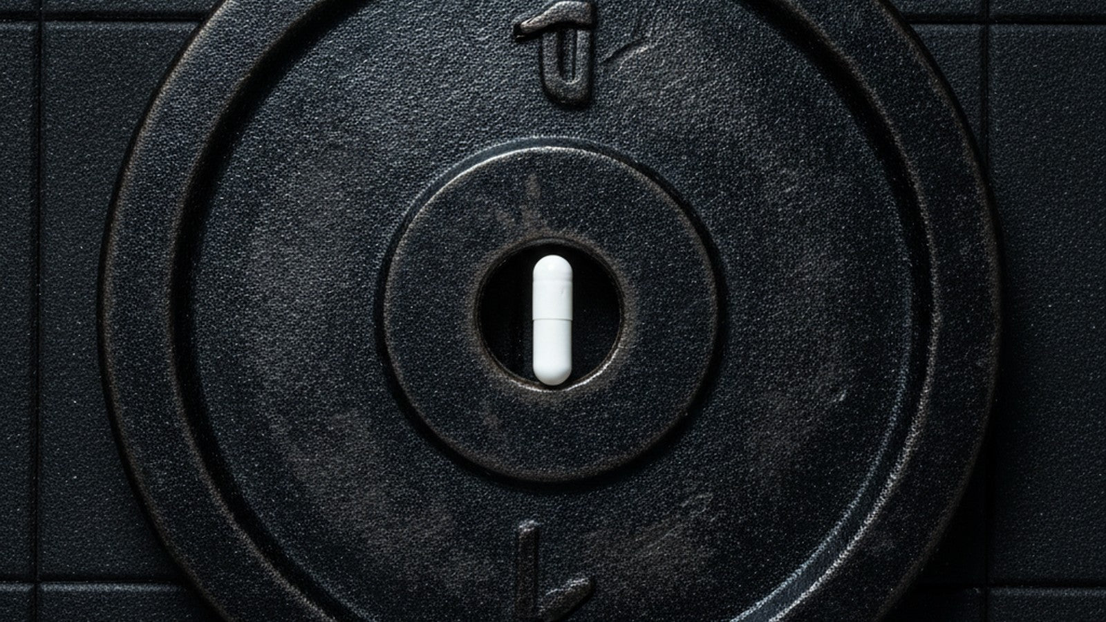 Single white supplement capsule on black weight plate