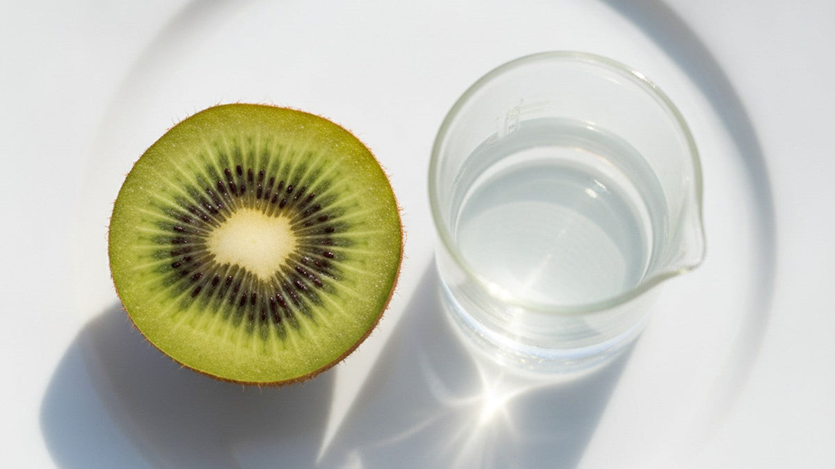 Sliced green kiwifruit beside laboratory beaker on white plate
