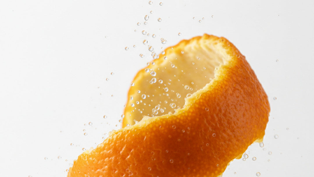 Orange peel being twisted and releasing essential oil spray