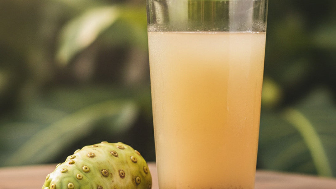 Glass of fermented noni juice next to whole noni fruit