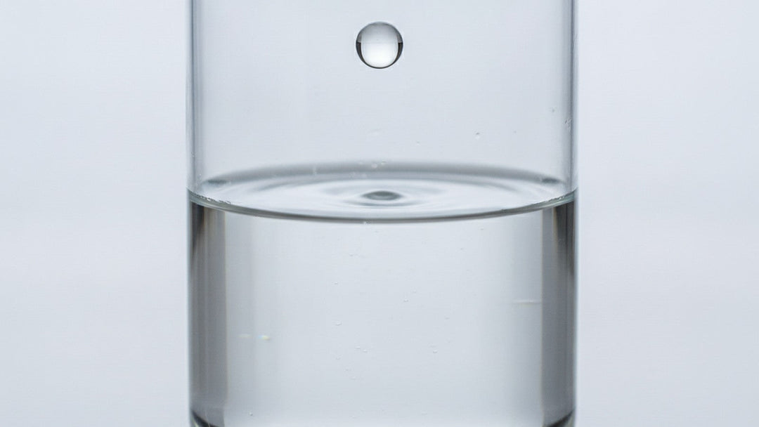 Water droplet falling toward beaker surface in laboratory setting