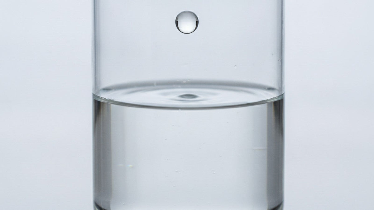 Water droplet falling toward beaker surface in laboratory setting
