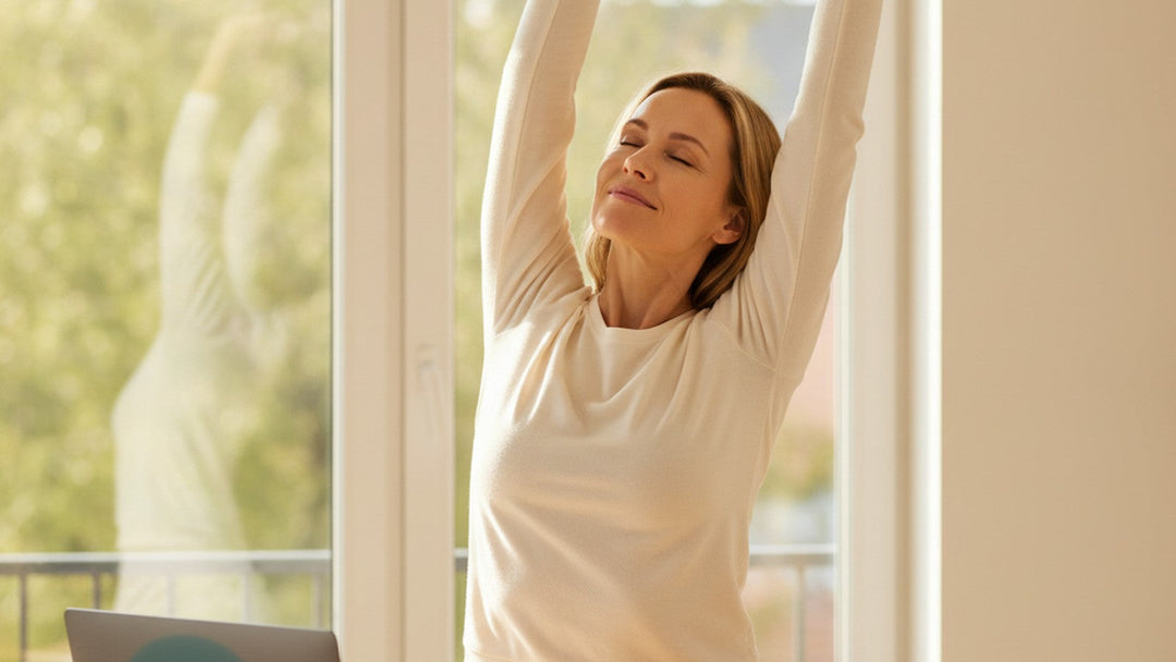 Woman stretching and refreshed at a sunlit home-office window in mid-afternoon