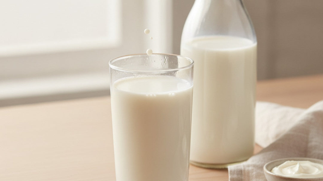 A tall glass of fresh milk beside a clear glass milk bottle in soft morning window light