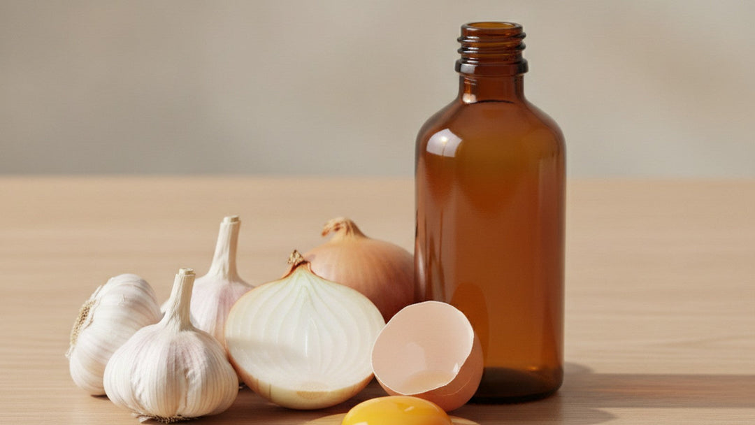 Amber glass supplement bottle beside fresh garlic, a halved white onion and a cracked egg on pale oak