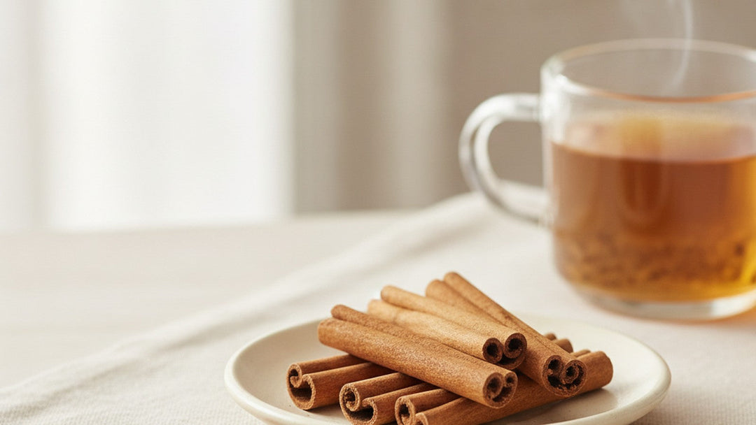 Ceylon cinnamon quills on a pale ceramic dish beside a glass mug of cinnamon tea in bright natural light