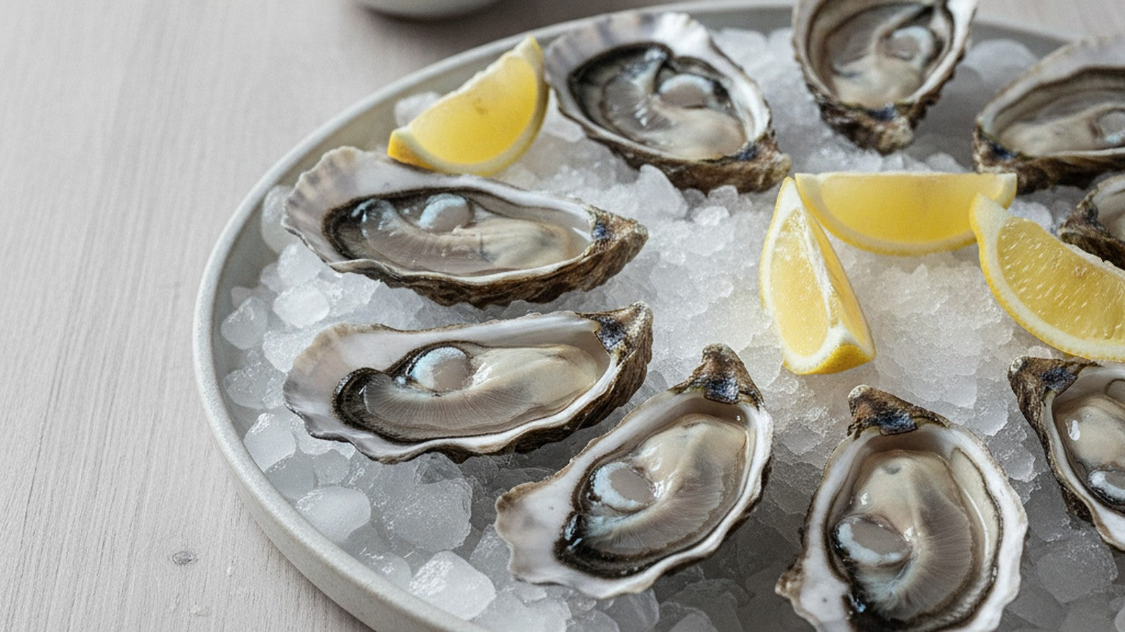 Fresh oysters on the half shell on crushed ice with lemon wedges on a pale ceramic platter